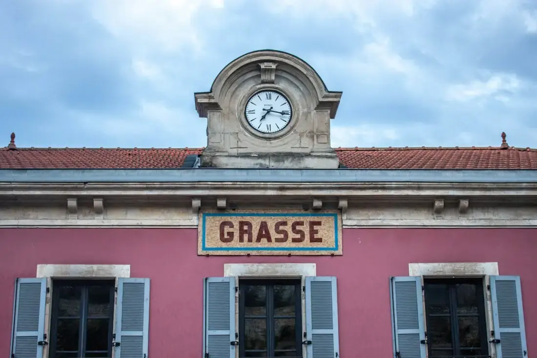 Façade rose surmontée d’une horloge, avec l’inscription Grasse